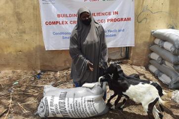 A smallholder farmer poses with goods and livestock received through the bricc program.