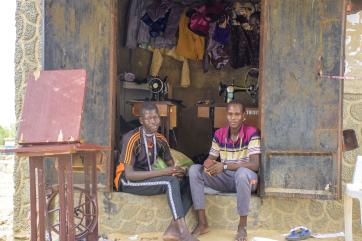 Two people sitting in front of their workshop.