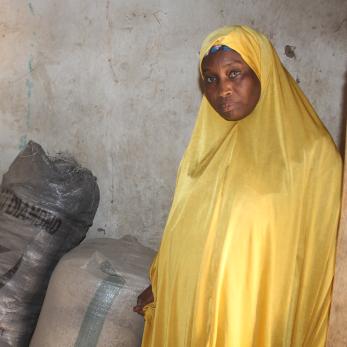 A person posing beside some bags of sorghum grains.