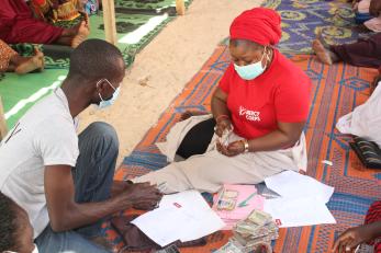 A mercy corps member counts cash while sitting on a floor mat. 