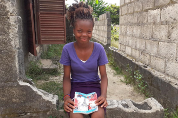 A young person smiles while holding an educational workbook.