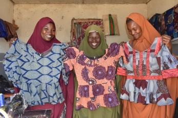 Three people holding up dresses and smiling.