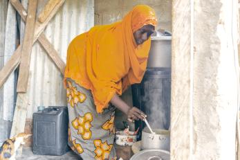 Nigerian woman bending over to stir a spoon in a cooking pot