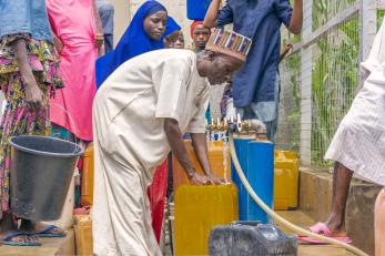 Nigerian man bending over to fill a bucket at an outdoor water pump