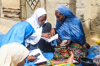 Two participants look in a ledger while counting money in nigeria.