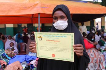 A participant holds a certificate of completion from a tailoring center training program. 