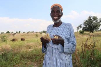 A farmer happily holds some produce they grew. 