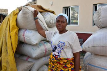 A person stands with sacks of grains in front of their small business.