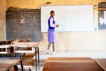 Nigerian student at whiteboard in empty classroom.