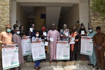 A group of people wearing personal protective equipment stand together while holding cards and posters displaying a code of conduct. 