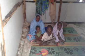 An adult sits on the ground with three children.