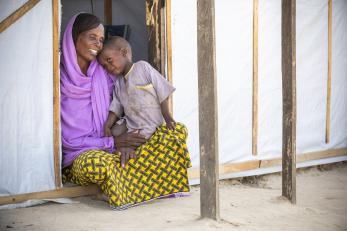 Mother and child sit in doorway of temporary shelter.