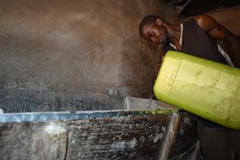 A person pours water into the kneading trough to prepare dough for baking.