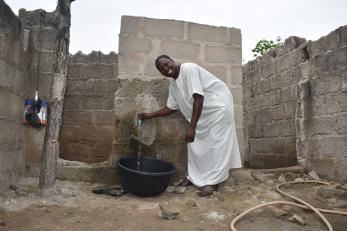 A person smiling while using a spigot from the tap in their house.