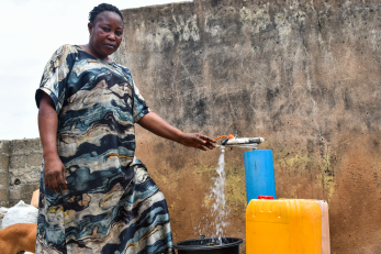 A person filling a bucket with water from a spigot at their home.