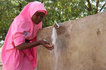 person holding hands under outdoor water spigot in Nigeria