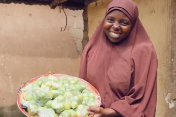 A person holding up a plate of fruit wrapped for vending.