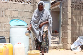 A person filling a bucket with clean water from their storage drum.