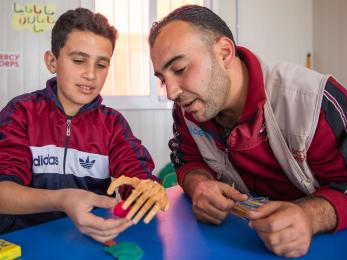 A young person works with Mercy Corps shadow teacher Saleh Alshalabi, learning how to strengthen his muscles and use his new prosthetic hand.