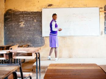 Nigerian student at whiteboard in empty classroom.