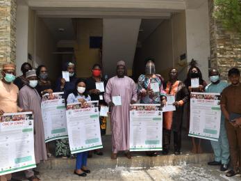 A group of people wearing personal protective equipment stand together while holding cards and posters displaying a code of conduct. 