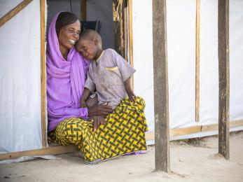 Mother and child sit in doorway of temporary shelter.
