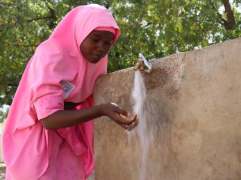 Person holding hands under outdoor water spigot in nigeria