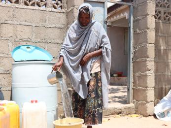 A person filling a bucket with clean water from their storage drum.