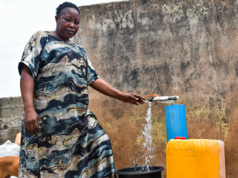 A person filling a bucket with water from a spigot at their home.
